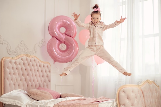 Photo heureuse petite fille en pyjama sur le lit avec un ballon anniversaire de bébé