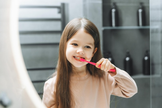 Heureuse petite fille se brosser les dents devant un miroir de salle de bain Hygiène du matin