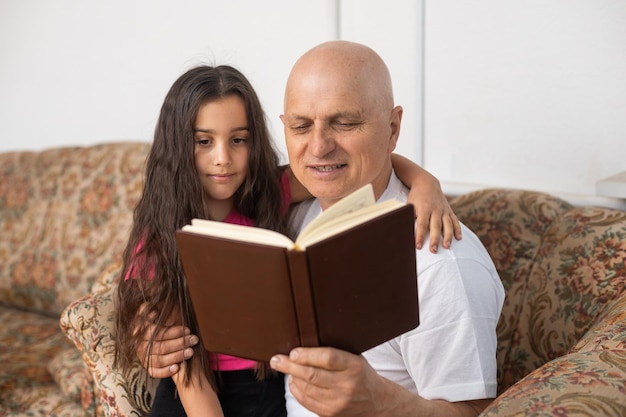 Heureuse petite fille avec son grand-père lisant un livre d'histoire à la maison