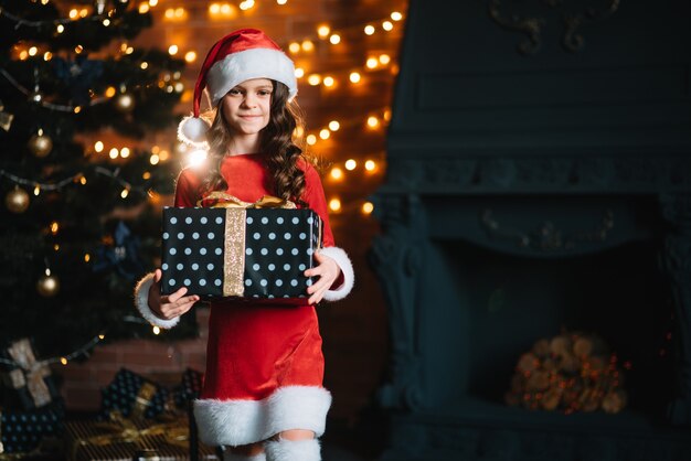 Heureuse petite fille souriante avec une boîte-cadeau près de l'arbre de Noël. Notion de Noël.