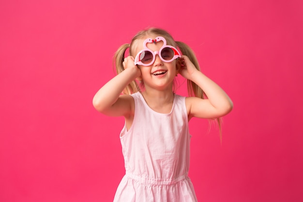 heureuse petite fille souriante dans des lunettes de soleil sur fond rose