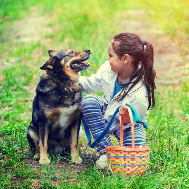 Heureuse petite fille souriante avec panier pique-nique assis avec le chien sur l'herbe
