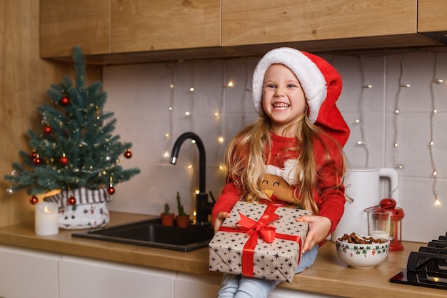 Heureuse petite fille tenant dans les mains une boîte-cadeau enveloppée sur le fond de l'arbre de Noël