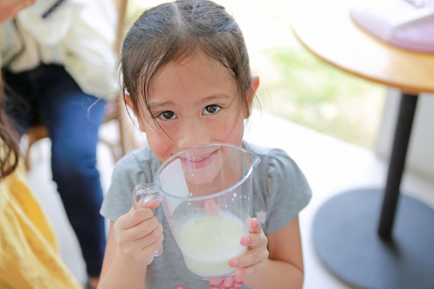 Heureuse petite fille tenant un verre de lait frais des vaches à la ferme de production laitière.