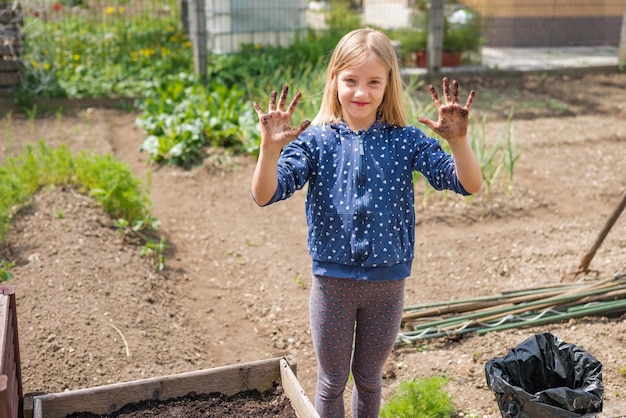 Heureuse petite fille travaillant au potager avec de la terre sur les mains