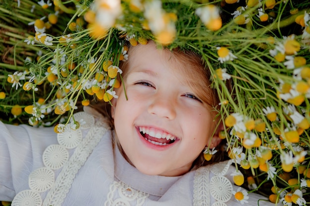 Heureuse petite fille vêtue d'une robe en coton se trouve dans un champ de marguerites en été au coucher du soleil. rires, vue d'en haut