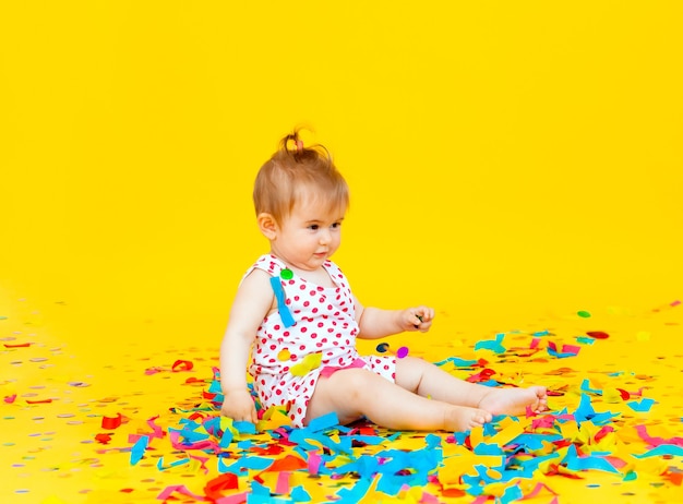 Heureuse petite fille vêtue d'une robe à pois attrape des confettis sur fond jaune. place pour le texte