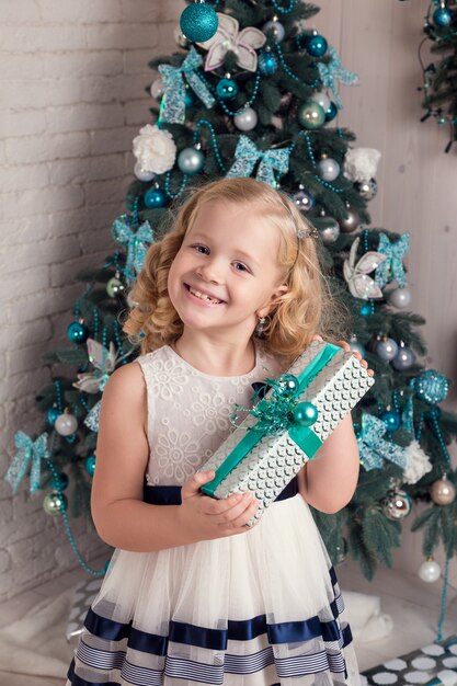 Heureuse petite fille vêtue d'une robe avec son cadeau de Noël