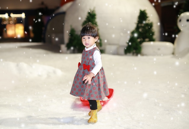 Heureuse petite fille vêtue d’une veste rouge - grise s’amuse dans la neige, l’hiver.