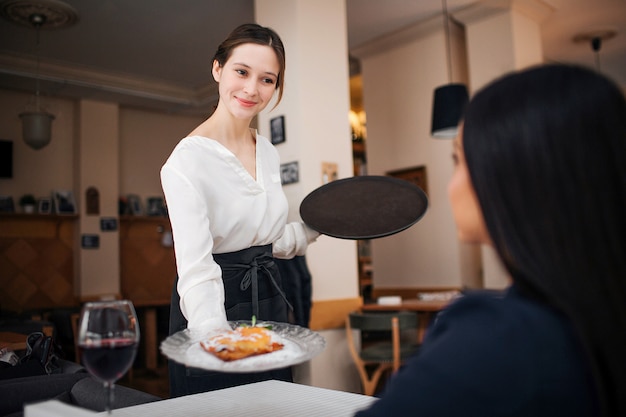 Heureuse et positive jeune serveuse se tient devant le client au restaurant