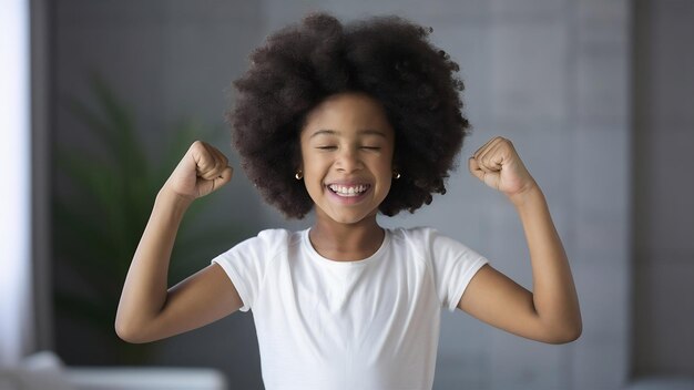 Heureuse et ravie, la fille afro serre les poings, ressent le triomphe, se réjouit de la victoire, ferme les yeux, sourit.