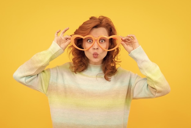 Heureuse rousse porte des lunettes de fête drôles sur la fête de fond jaune