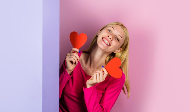 Heureuse saint valentin femme blonde souriante avec deux coeurs en papier rouge symbole d'amour