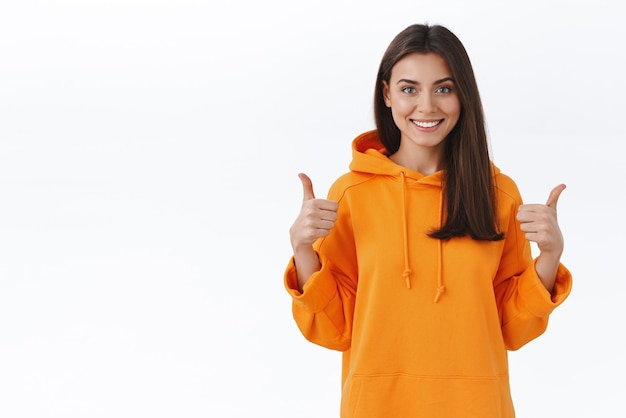 Heureuse et satisfaite belle étudiante en sweat à capuche orange recommander un cours en ligne louange excellent travail montrer le pouce levé et souriant ravi laisser un avis positif fond blanc