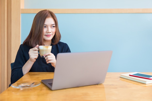 Heureuse séduisante jeune femme asiatique profitant de son café pendant le travail