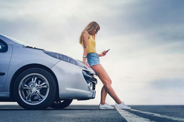 Heureuse seule jeune femme voyageuse sur la route avec une voiture avec la main tenant un téléphone portable Voiture de voyageur dans le concept de voyage sur la route d'été rechercher la route du réseau Lily loin de la ville