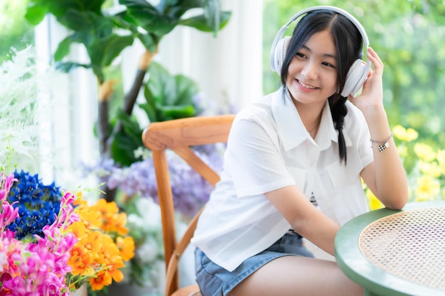 Photo heureuse de sourires mignons asiatiques de jeunes attirantes mignonne petite fille portant des écouteurs sans fil blancs et écoutant de la musique appréciant l'audio préféré au café en vacances dans un café