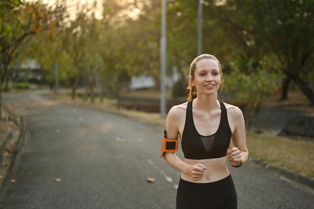 Heureuse sportive portant un brassard pour faire du jogging sur smartphone dans un parc tropical Sport et concept de mode de vie sain