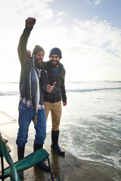 Photo heureuse surprise et les gens avec des poissons à l'eau avec fierté pour la capture de thon sur le quai au coucher du soleil les amis de la pêche et les pêcheurs sourient de choc au succès dans la nature en mer en vacances ou en vacances