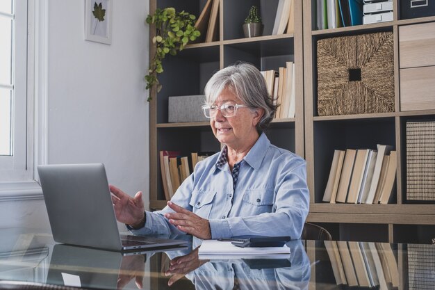 Heureuse vieille femme d'affaires caucasienne souriante travaillant en ligne en regardant un podcast de webinaires sur un ordinateur portable et en apprenant la conférence de cours d'éducation prendre des notes s'asseoir au bureau, concept d'apprentissage en ligne