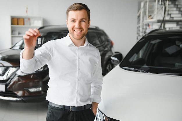 Heureux acheteur tenant des clés près de la voiture devant le bâtiment moderne d'avtosalon