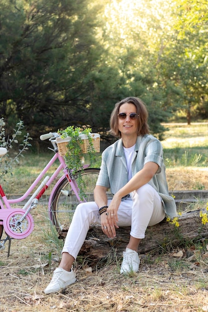 Heureux adolescent similing aux cheveux longs regardant vers l'appareil photo profitant de son temps libre avec son nouveau vélo rose rétro