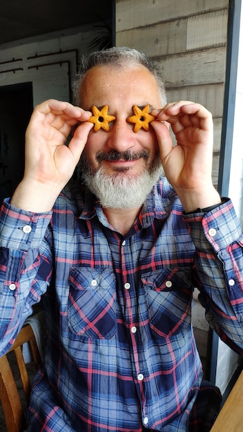 Heureux adulte barbu homme détient deux biscuits en forme d'étoiles devant ses yeux, dépeint des lunettes, un concept amusant avec des biscuits