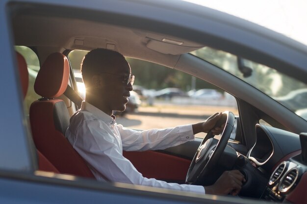 Photo heureux afro-américain conduisant une voiture avec un téléphone, en été