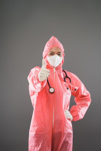 Heureux agent de santé féminin debout portant un EPI et un masque avec les pouces vers le haut et une main sur la taille