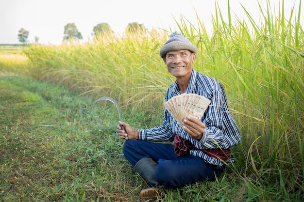 Heureux agriculteur asiatique avec un visage souriant main tenant de l'argent dans le concept de subvention en espèces de la ferme de riz