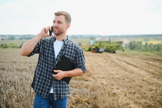 Heureux agriculteur fièrement debout dans un champ Conducteur de moissonneuse-batteuse allant récolter une riche récolte de blé Agronome portant une chemise en flanelle regardant la caméra sur une terre agricole