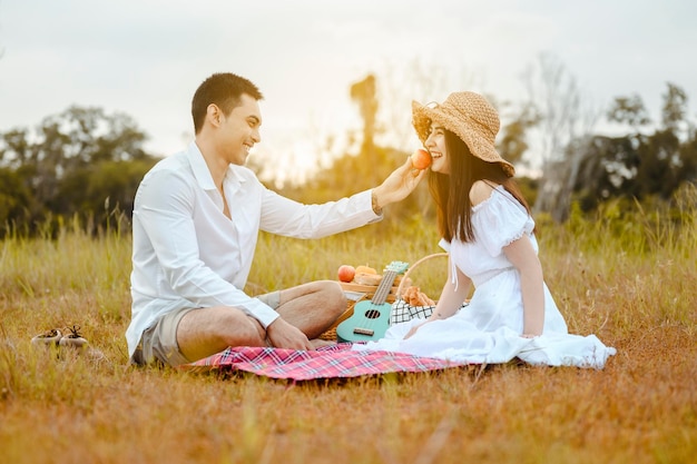 Heureux amants assis sur la prairie se regardant avec tendresse. Les hommes donnent des pommes aux femmes. Ils se regardent avec amour et sourires.