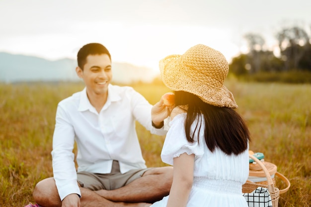 Heureux amants assis sur la prairie se regardant avec tendresse. Les hommes donnent des pommes aux femmes. Ils se regardent avec amour et sourires.