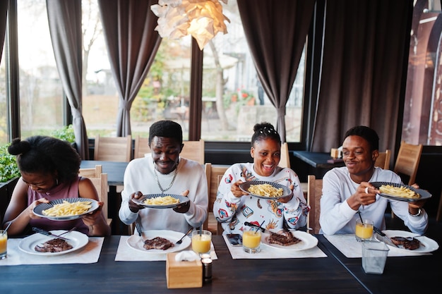 Heureux amis africains assis à discuter au café et manger de la nourriture Groupe de peuples noirs se réunissant au restaurant et dînant Ils tiennent des assiettes avec des frites