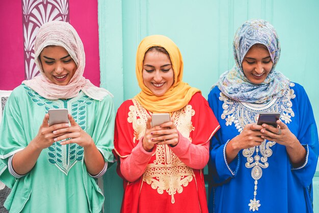 Heureux amis arabes utilisant des smartphones en plein air - Jeunes filles islamiques s'amusant avec la nouvelle technologie de tendance - Concept d'influence et d'amitié - Focus sur les visages