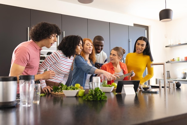 Photo heureux amis divers cuisinant ensemble et utilisant une tablette dans la cuisine