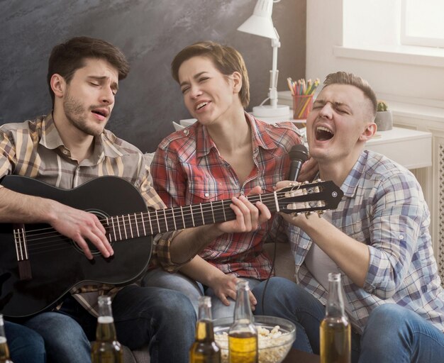 Heureux amis faisant la fête, jouant de la guitare et chantant à la maison