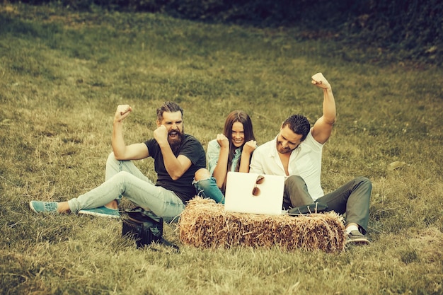 Heureux amis gens jolie fille et beaux hommes avec un ordinateur portable lèvent les mains du geste du gagnant à l'extérieur sur fond naturel