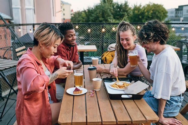 Heureux amis interculturels ayant une restauration rapide et des boissons dans un café en plein air