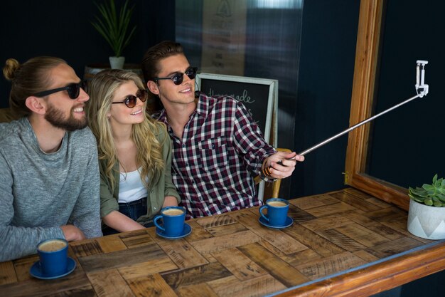 Heureux amis prenant selfie avec monopode à table à la cafétéria