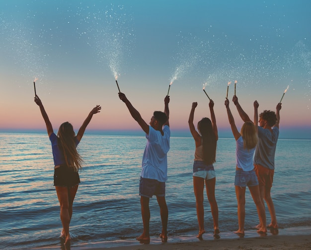 Heureux amis souriants à la plage avec des bougies scintillantes à la main