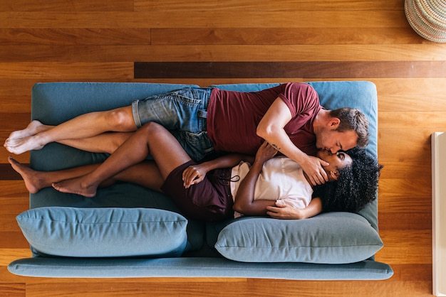 Photo heureux amoureux multiethniques reposant sur le canapé et s'embrassant à la maison