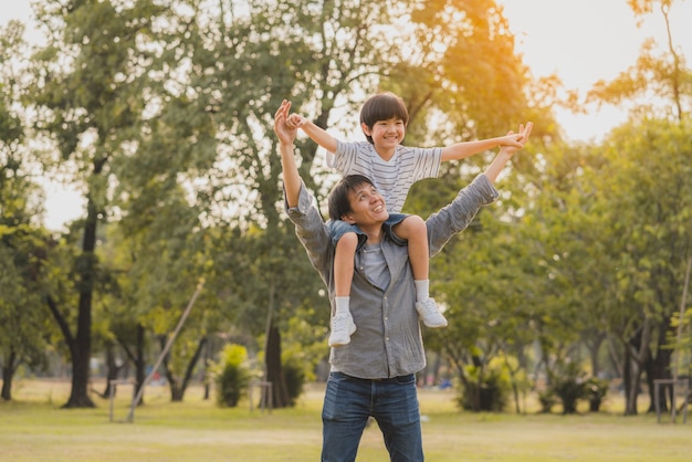 Heureux et amusant père asiatique donnant son fils monter sur ses épaules comme voler dans le parc