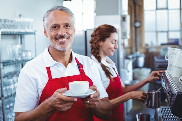 Heureux barista souriant à la caméra et tenant une tasse de café