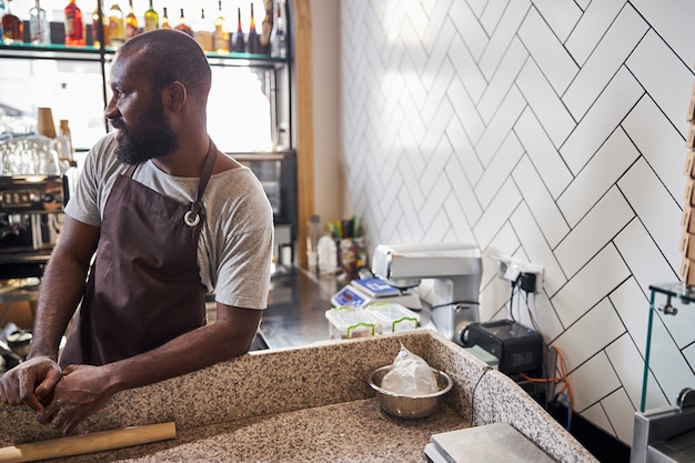 Heureux beau chef barbu en tablier travaille dans une cuisine ouverte et prépare des pizzas pour les invités