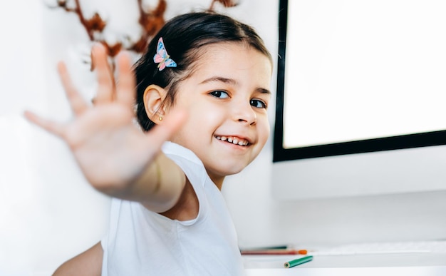 Heureux beau gosse fille faisant le geste cinq haut assis à côté de l'ordinateur à la maison Adorable enfant assis à une table dans la salle d'apprentissage