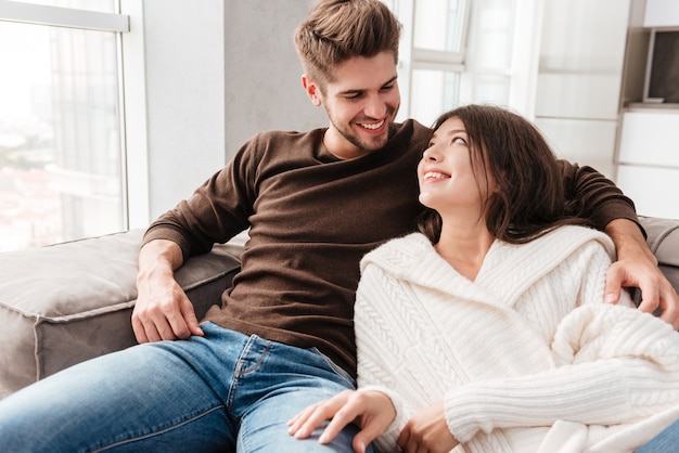 Heureux beau jeune couple assis sur le canapé à la maison ensemble