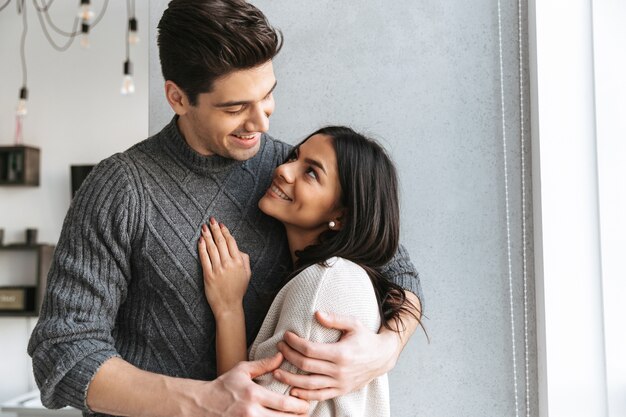 Heureux beau jeune couple debout à la fenêtre à la maison