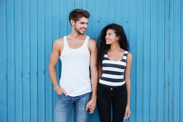 Heureux beau jeune couple debout et tenant la main sur le mur bleu