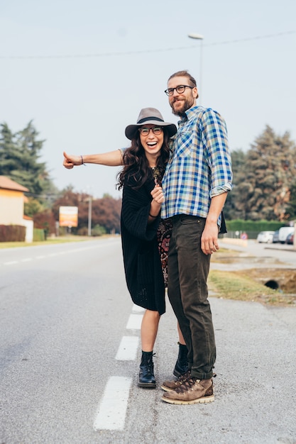 Heureux beau jeune couple faisant de l'auto-stop en plein air s'amusant à travers